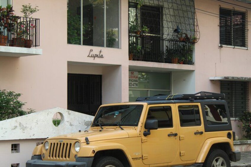 A yellow Jeep parked in front of a building with a balcony and a sign that reads 'Lupita.' 3