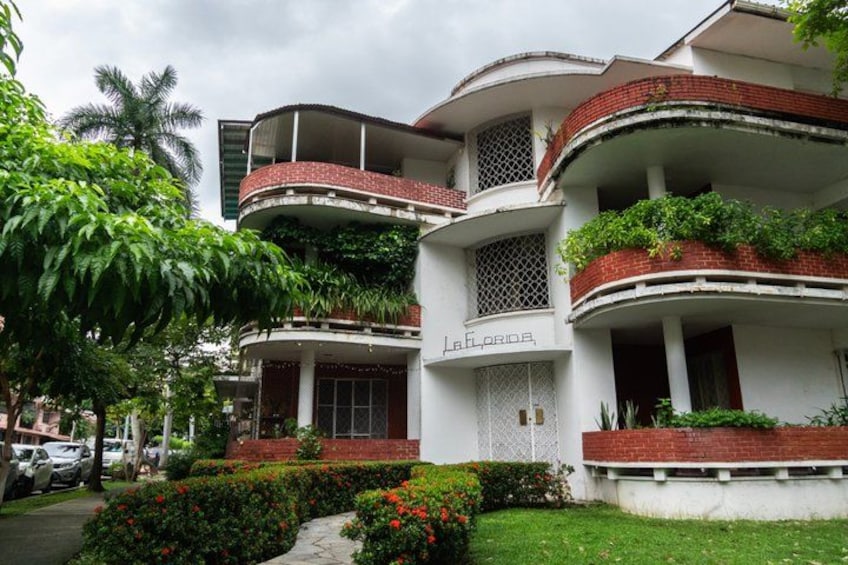 A multi-story building with balconies, lush greenery, and a clear sky. 1