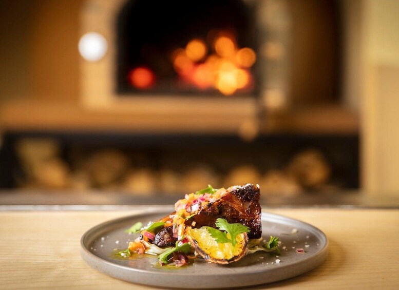 A plate of food with a piece of meat, vegetables, and a garnish, in front of a blurred fireplace. 4