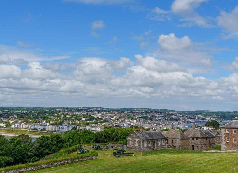 A coastal town with historic stone buildings, a green park, and a view of the sea and distant hills. 5