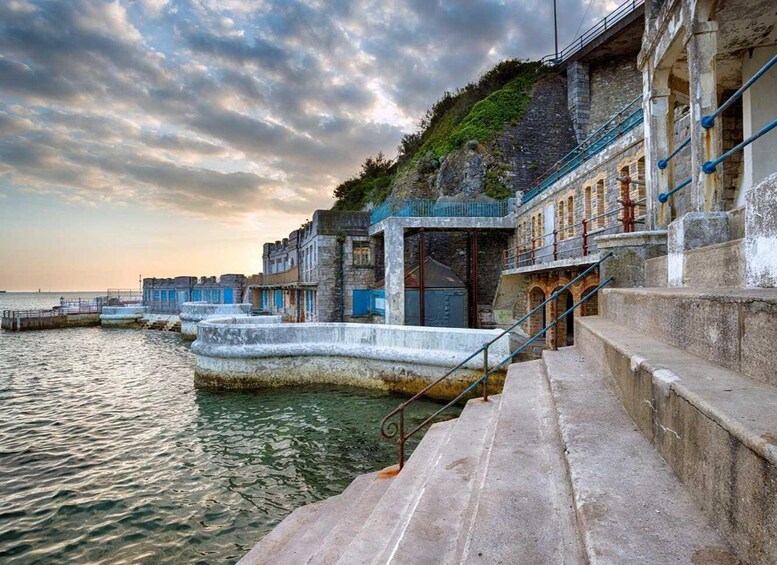 A coastal stone staircase leading to a building with blue shutters, overlooking calm waters. 1