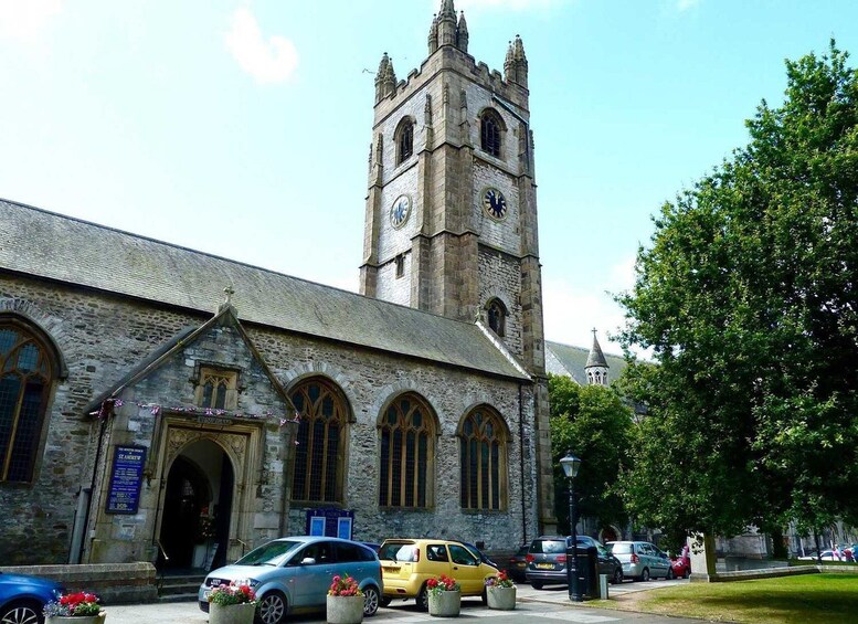 A historic stone building with a clock tower, parked cars, and a tree. 3
