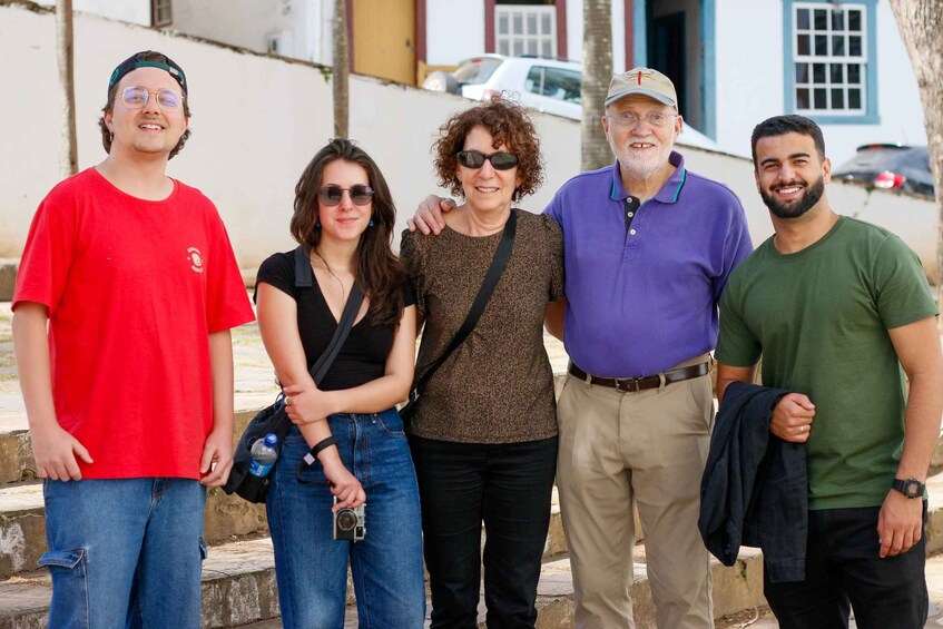 A group of people standing on a sidewalk with buildings and parked cars in the background. 3