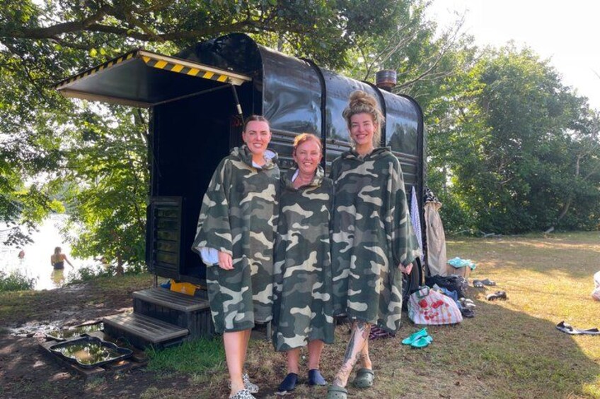 Two people in camouflage clothing standing in front of a black trailer with a small porch. 1