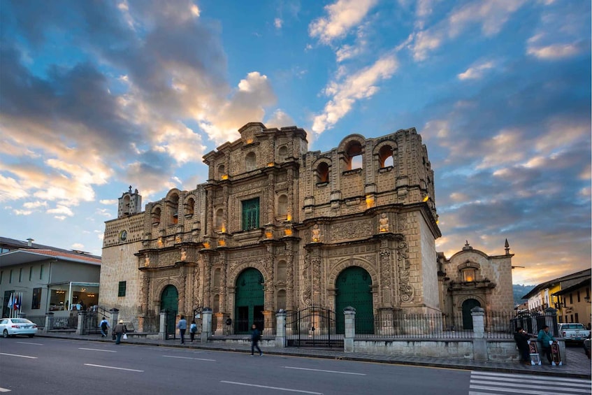 A historic building with ornate architecture and green doors, set against a backdrop of a cloudy sky. 1