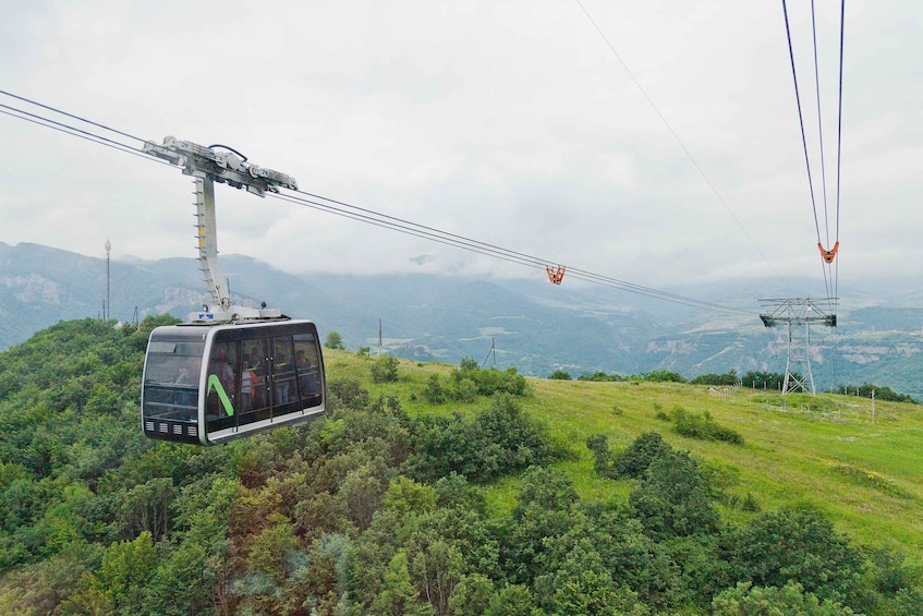 A cable car system with a cable car in motion, a mountainous landscape, and a power line tower in the background. 2