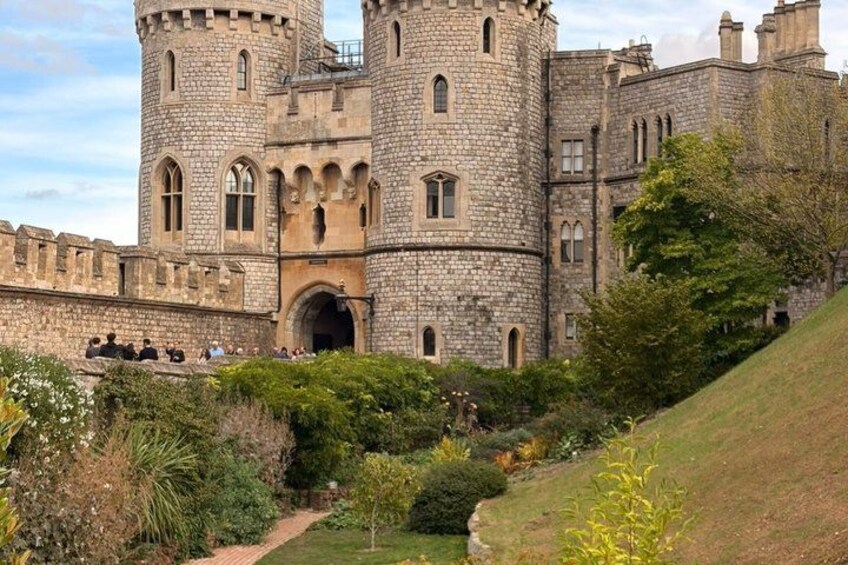 A historic stone castle with a central tower, surrounded by well-maintained gardens and a grassy hill. 4