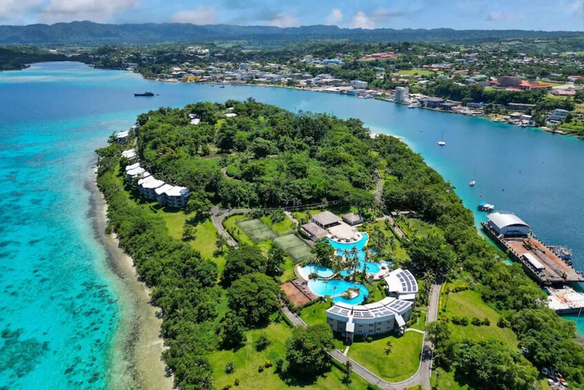 Vue aérienne d’une île tropicale avec un complexe hôtelier, des eaux turquoise et limpides, et une petite ville en arrière-plan. 2
