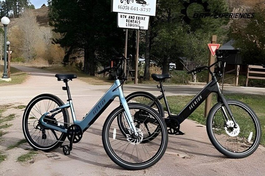 Two bicycles parked on a paved path with a sign in the background. 1