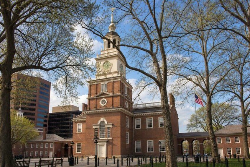 A historic brick building with a clock tower, surrounded by trees and a flag. 1