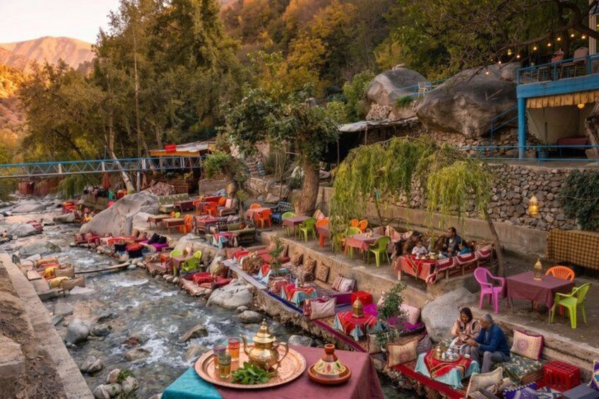 A riverside restaurant with outdoor seating, surrounded by trees and rocks. 2