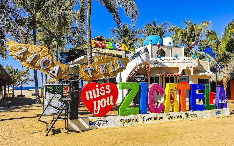 Un edificio colorido con letras grandes que deletrean 'ZICATELLA' y 'Puerto Escondido, Baja California, México' en su fachada. 1