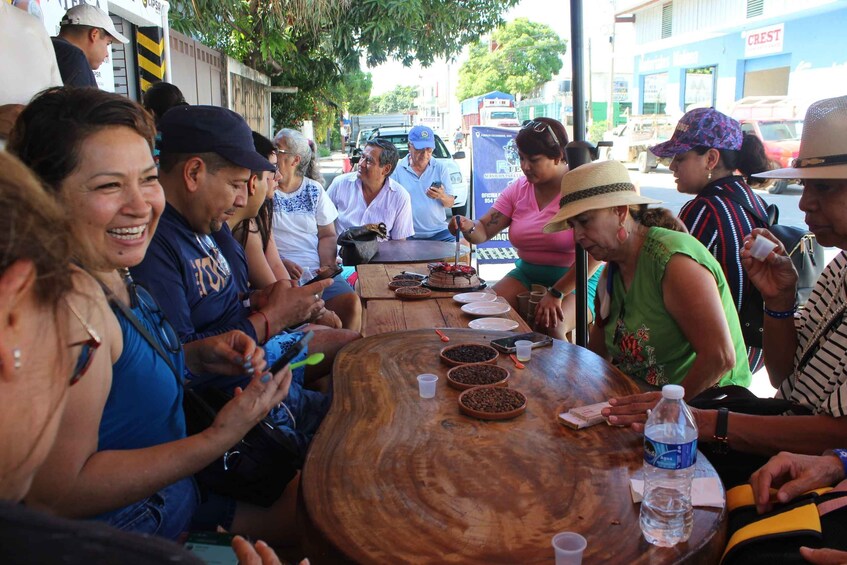 Un grupo de personas sentadas alrededor de una mesa de madera al aire libre, conversando y usando teléfonos móviles. 4