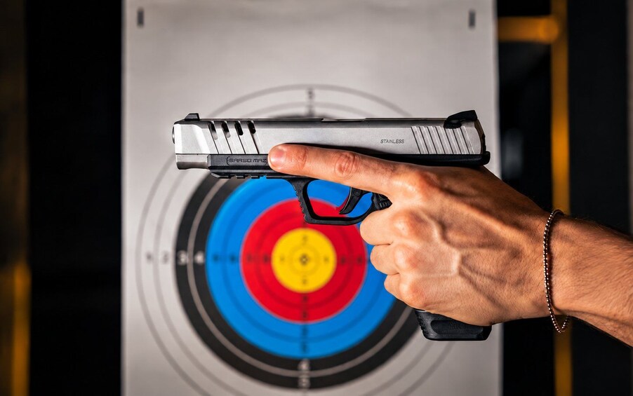 A hand holding a handgun with a target in the background. 2