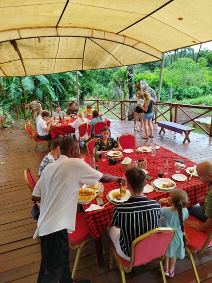 Un espacio al aire libre para comer con gente sentada en mesas bajo un toldo, rodeado de vegetación. 2