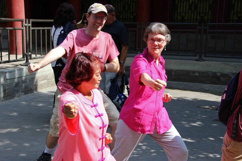 Two people in pink shirts performing a martial arts move outdoors. 1