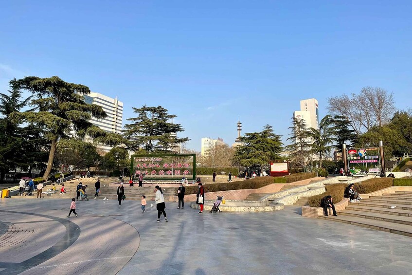 A public square with people walking, a stage with a banner, and modern buildings in the background. 4