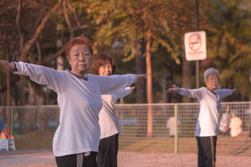 Three individuals performing Tai Chi in an outdoor setting with trees and a no-smoking sign in the background. 5