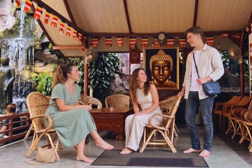 A covered outdoor area with wicker furniture, a Buddha statue, and a waterfall. 3