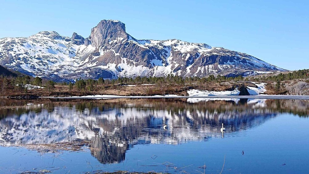 Une chaîne de montagnes aux sommets enneigés, un lac paisible qui reflète les montagnes et un ciel bleu clair. 5