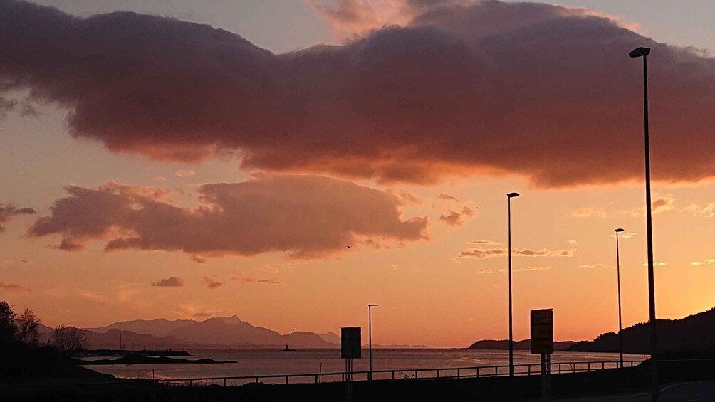 Un coucher de soleil sur une étendue d’eau, avec des montagnes à l’horizon et des lampadaires le long de la rive. 3