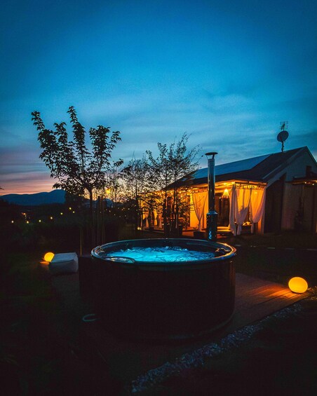 Un jacuzzi rodeado de árboles, una casa con porche y un atardecer al fondo. 4