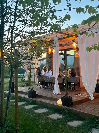Un área de comedor al aire libre con mesas y sillas de madera, rodeada de follaje y cortinas blancas. 5