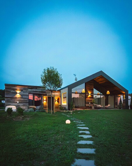 Una casa moderna con fachada de madera, un gran árbol en el frente y un sendero de piedra que lleva a la entrada. 1