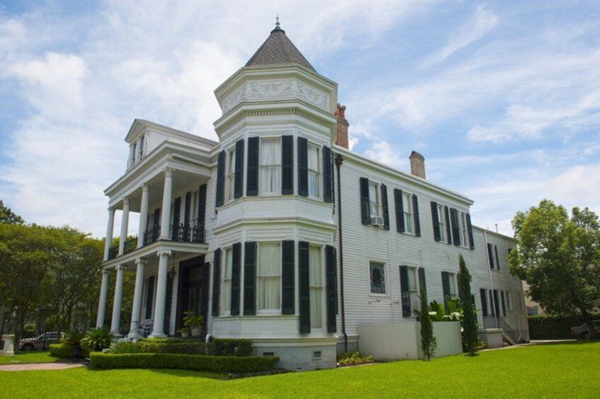 A large, white, two-story house with a turret and columns, surrounded by a well-maintained lawn and trees. 5