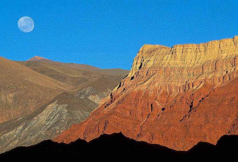 Eine gebirgige Landschaft mit einer markanten Klippe und einem Vollmond am Himmel. 1