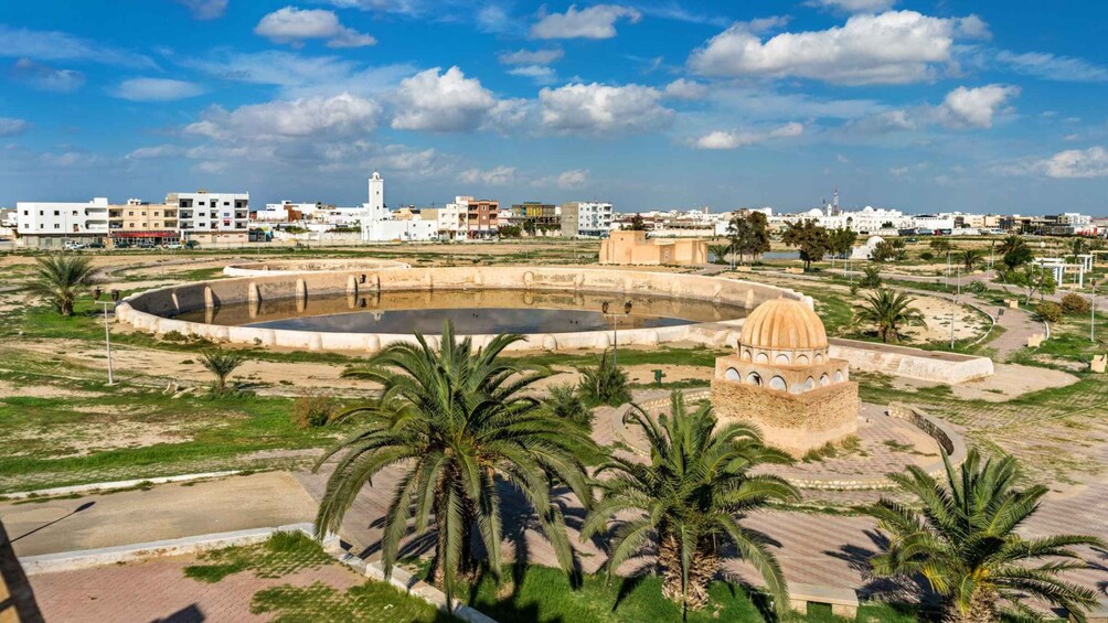 Una fuente circular con una estructura en forma de cúpula, palmeras y edificios al fondo. 4