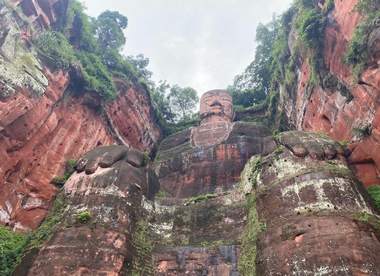 A large rock formation with a carved face at the top, surrounded by red cliffs and greenery. 5