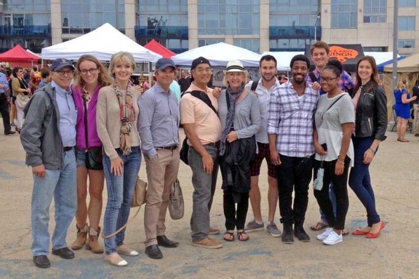 A group of people posing for a photo in an outdoor setting with tents and buildings in the background. 3