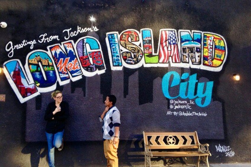 A wall with 'Greetings From Jackson's Long Island City' and a bench. 5