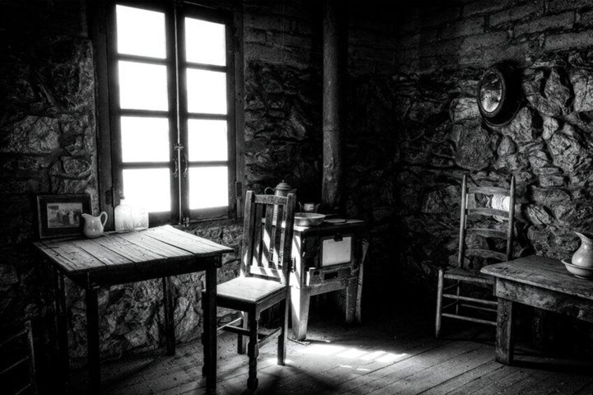 A rustic stone-walled room with wooden furniture, including a table and chairs, and a window allowing natural light to enter. 5