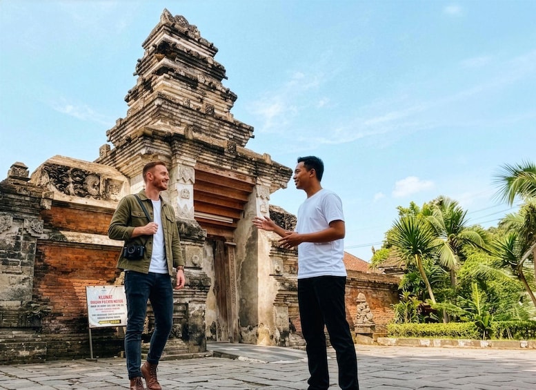 Two people conversing in front of an ancient temple with intricate carvings and a signboard. 5