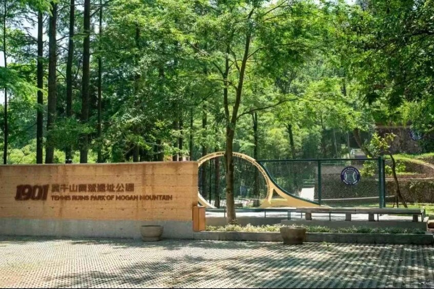 A park entrance with a wooden sign, a metal fence, and trees in the background. 2