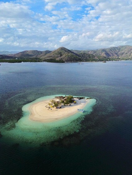 Luchtbeeld van een klein eiland met helder turquoise water, een zandstrand en enkele verspreide gebouwen. 1