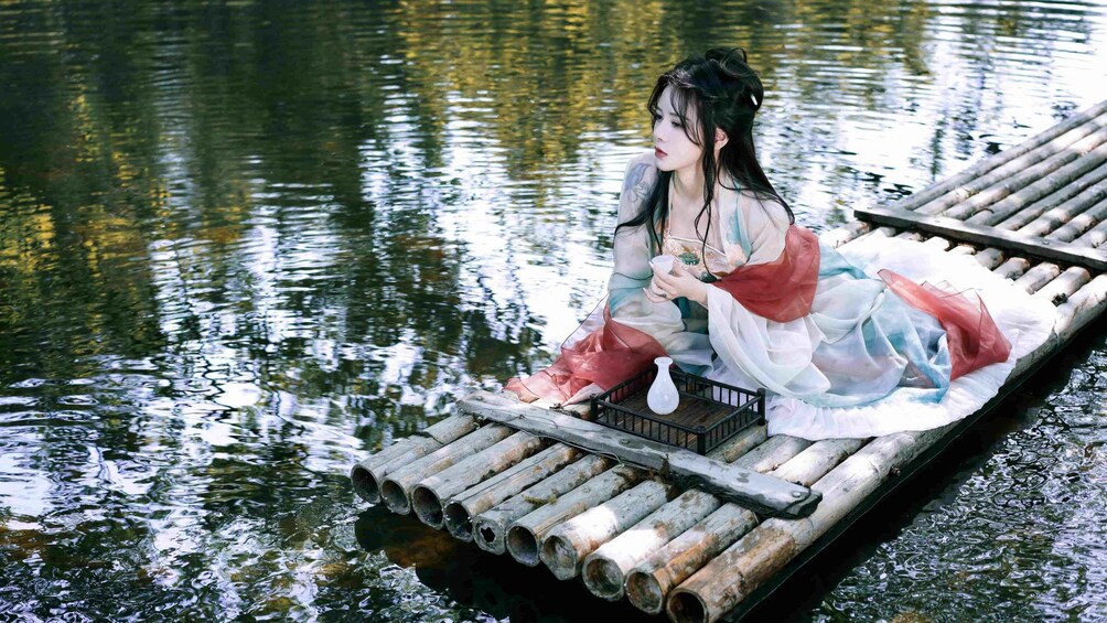 A person in traditional attire sitting on a bamboo raft in a body of water. 2