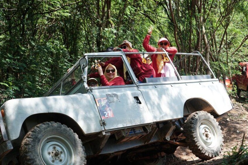 A white off-road vehicle with four passengers in a forested area. 4