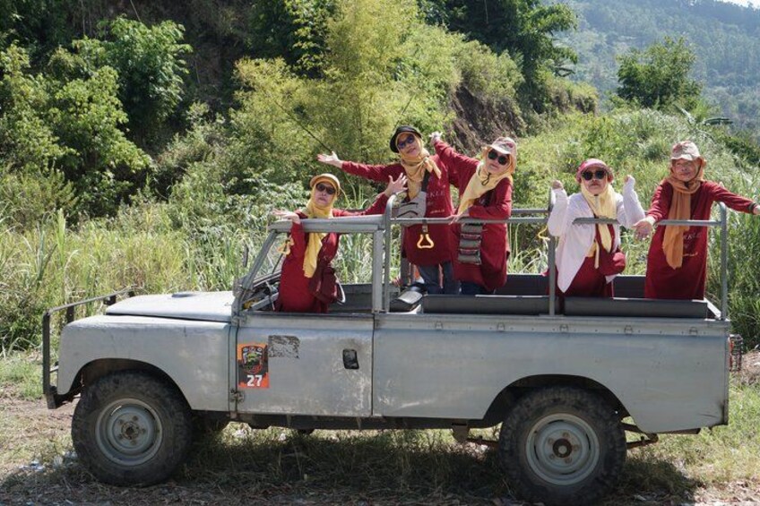 A group of people in red and white attire on a gray off-road vehicle in a natural setting with greenery and hills. 3