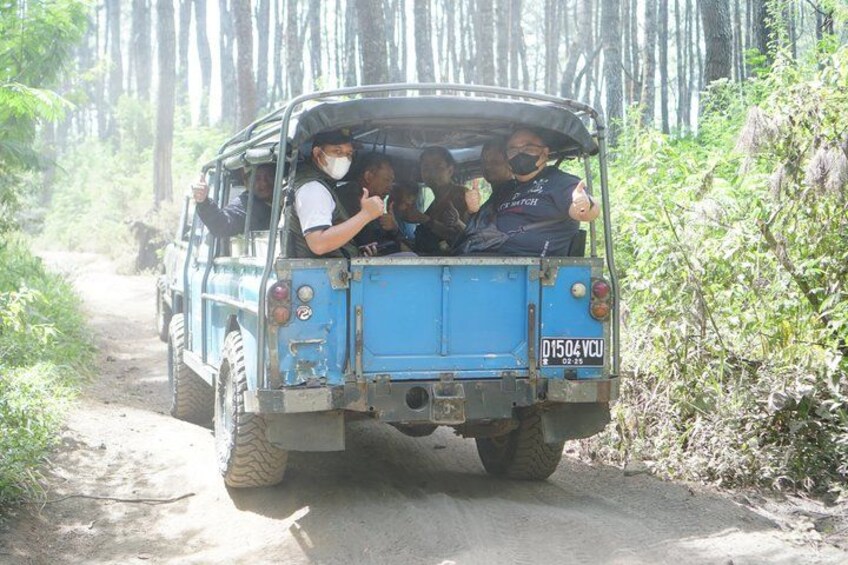 A blue vehicle with passengers, driving on a dirt road surrounded by trees. 5