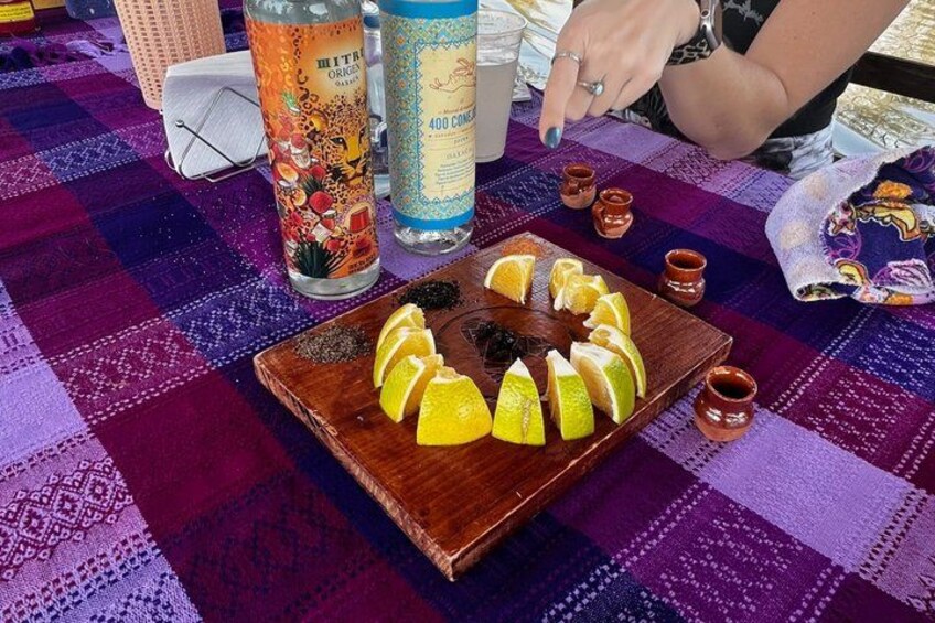 A table with a checkered tablecloth, a plate of sliced lemons, a bottle of orange juice, and a glass of water. 4