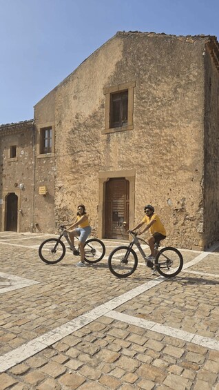 Two people on bicycles in front of a historic building with a cobblestone street. 2