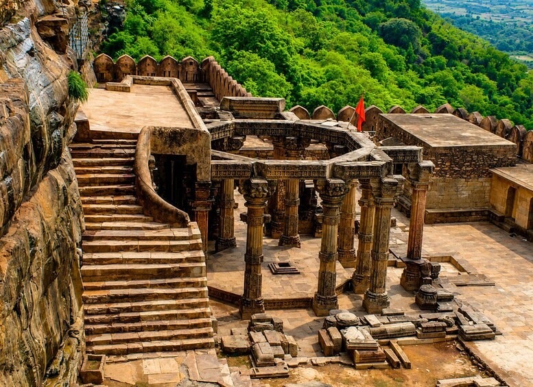 Ancient stone structures with intricate carvings, a staircase leading up to a platform, and a lush green forest in the background. 2