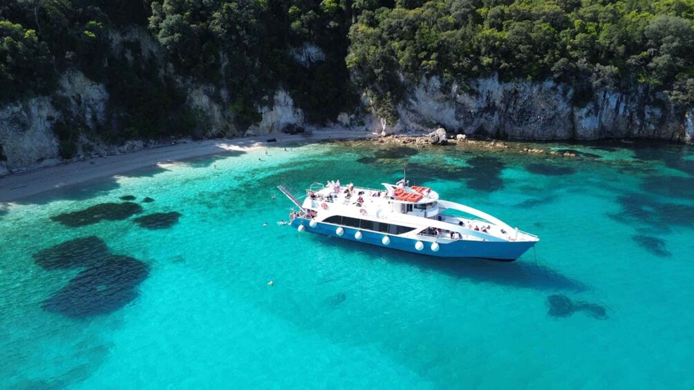 A boat on turquoise waters with a rocky coastline and dense greenery in the background. 1