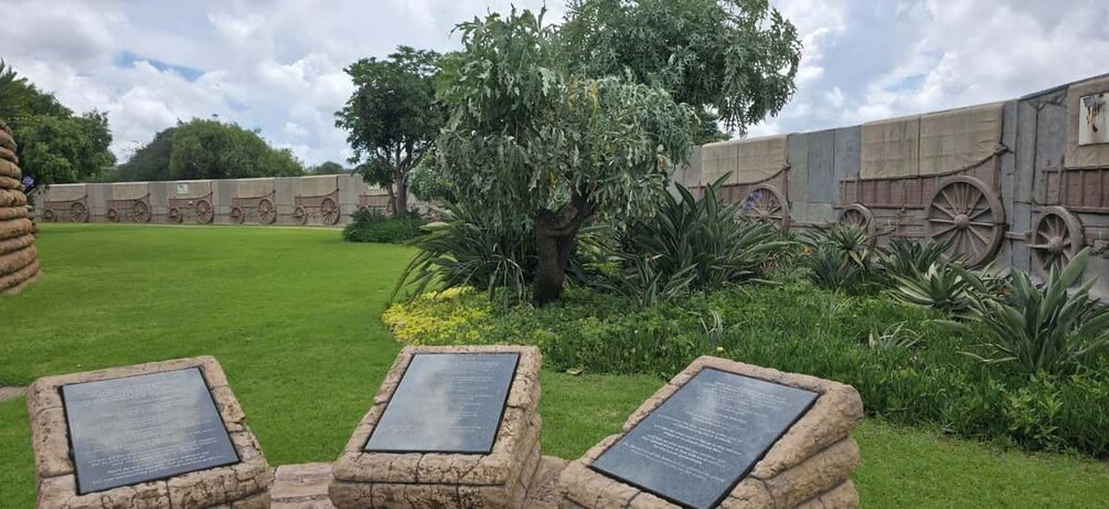 Un monumento con placas de piedra, un árbol y un muro con ruedas de carretilla. 4