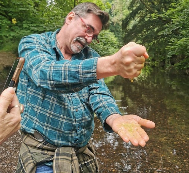 A person holding a smartphone and a fishing rod, standing by a river. 2