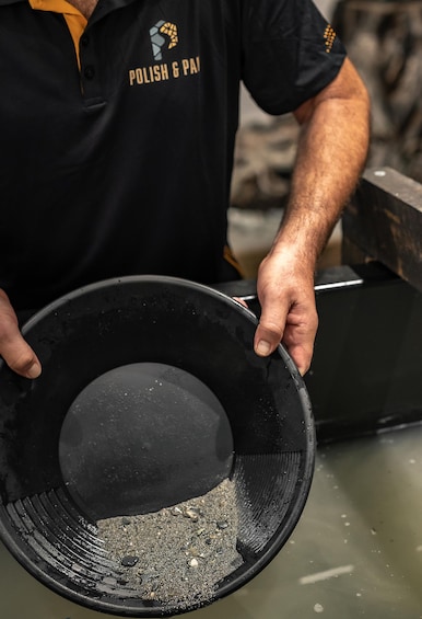Une personne tenant un objet circulaire noir à la surface texturée, qui pourrait être un outil ou un récipient, dans un atelier ou un environnement industriel. 2