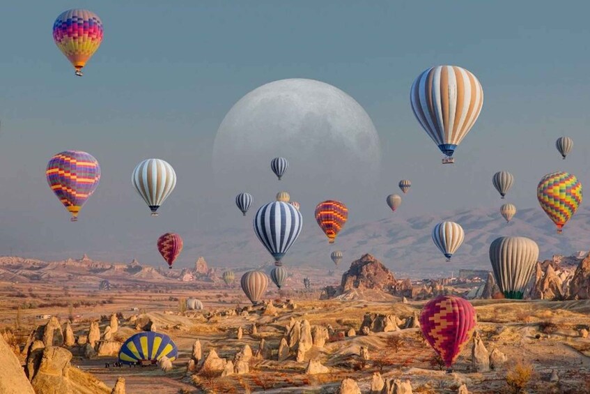 Eine Landschaft mit zahlreichen Heißluftballons in verschiedenen Farben und Mustern, einem großen Mond am Himmel und einer felsigen Landschaft mit einzigartigen Felsformationen. 1